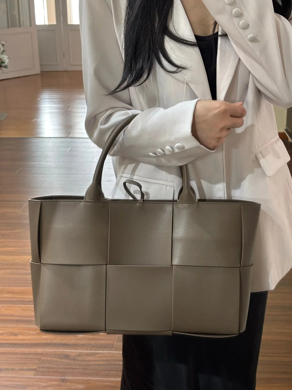 Woman holding large taupe quilted leather tote bag with top handles, minimalist and elegant design
