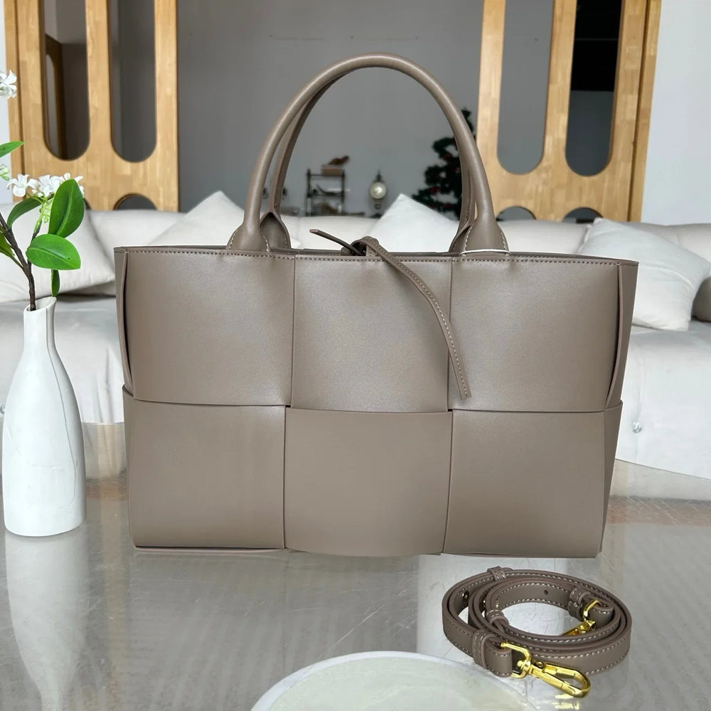 Taupe quilted leather tote bag with top handles and detachable strap on a modern table.