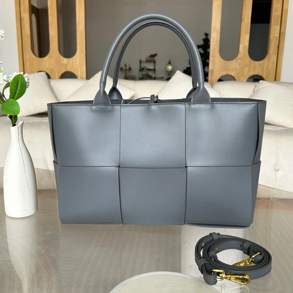 Quilted large grey leather tote bag with top handles and detachable shoulder strap on table
