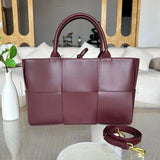 Large quilted leather tote bag in burgundy with top handles and detachable shoulder strap on table