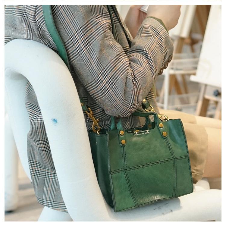 Green full grain leather small handbag with top handles and gold hardware, worn crossbody.