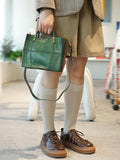 Woman holding a green full grain leather shoulder bag with crossbody strap, fashion purse