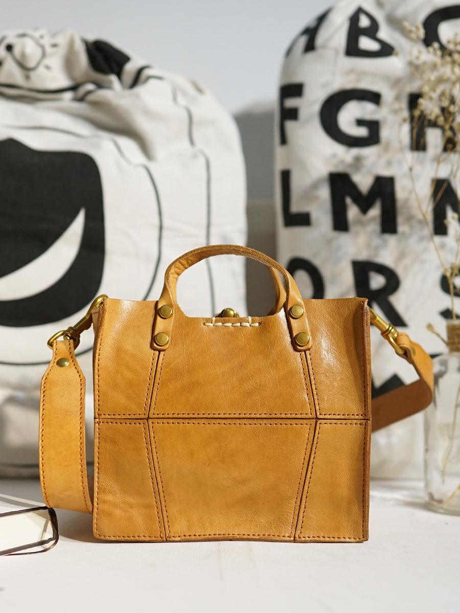 Tan full grain leather small handbag with shoulder strap, minimalist design, on table indoors