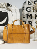 Tan full grain leather small handbag with shoulder strap, minimalist design, on table indoors