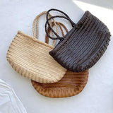 Three woven Italian leather tote bags in beige, brown, and dark brown on a light surface
