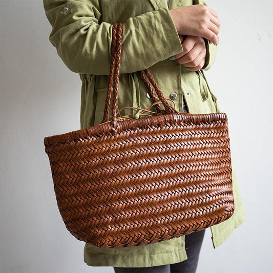 Hand holding a large brown woven leather tote bag with braided handles.