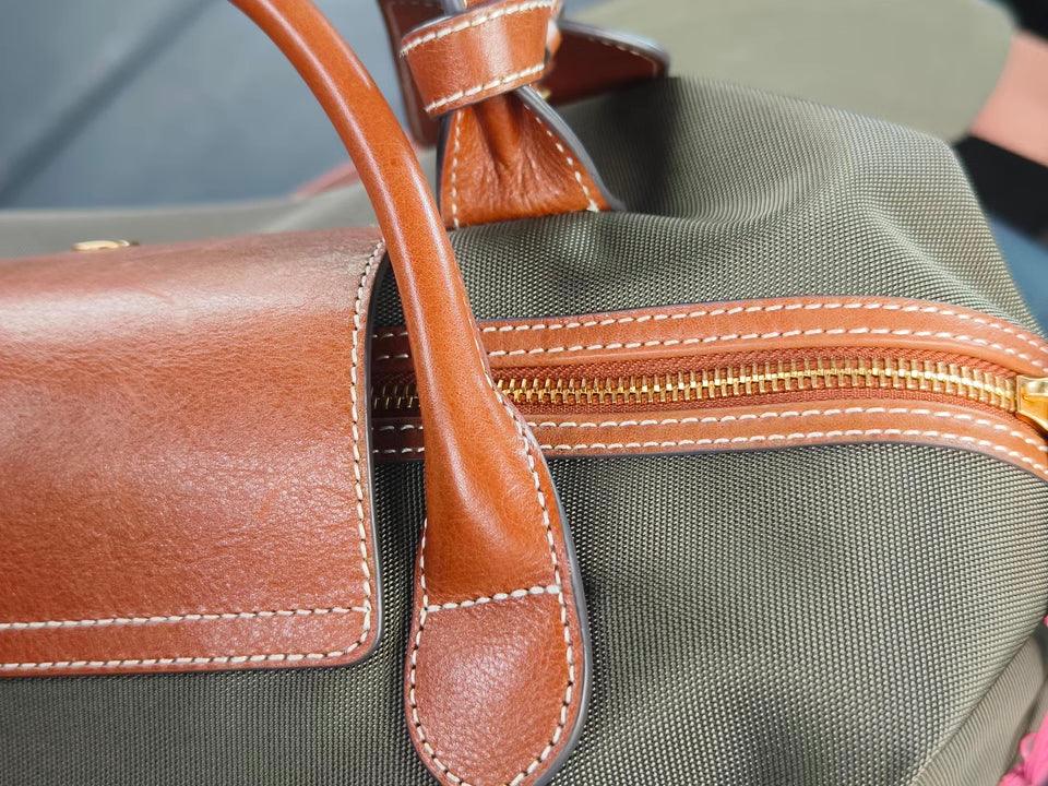 Close-up of a waterproof nylon tote bag with brown cowhide leather handles and gold zipper