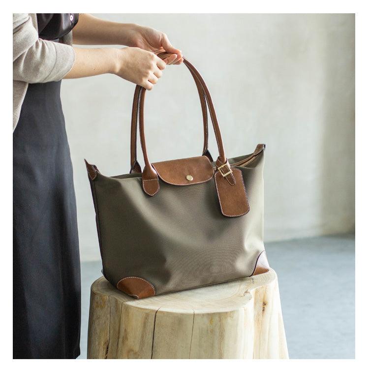 Waterproof taupe nylon tote bag with brown cowhide leather handles and accents on a wooden stool