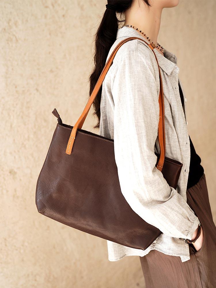Woman carrying large black full-grain leather tote bag with brown handles