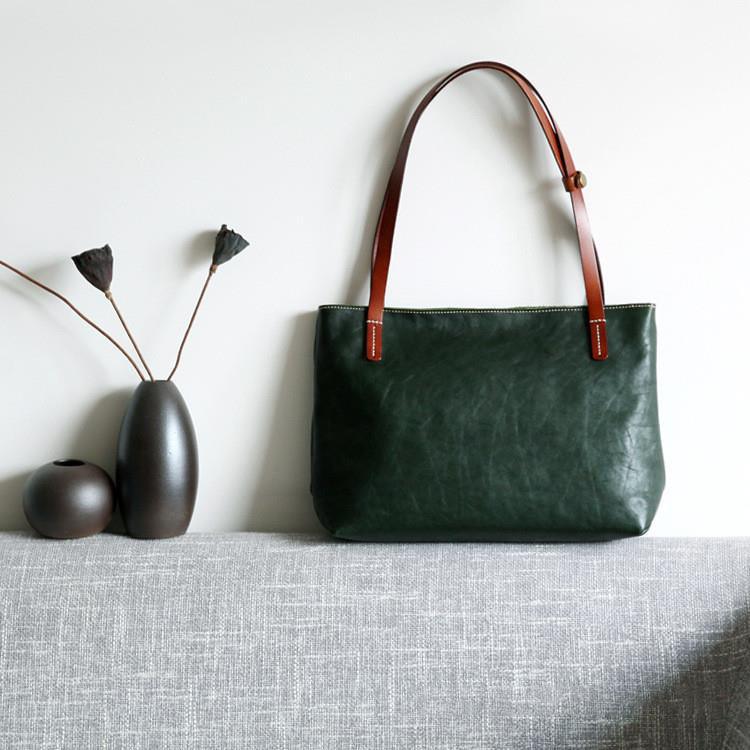 Black full-grain leather tote bag with brown handles, handcrafted, displayed on a light couch.