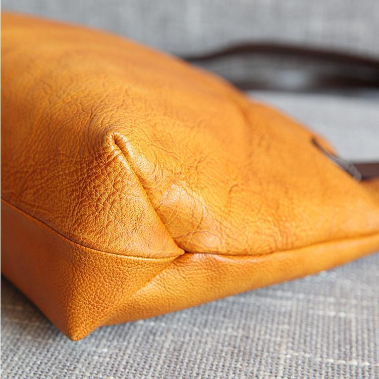 Close-up of an orange full grain leather tote bag corner on a textured fabric surface.