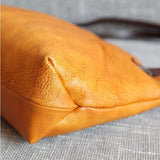 Close-up of an orange full grain leather tote bag corner on a textured fabric surface.