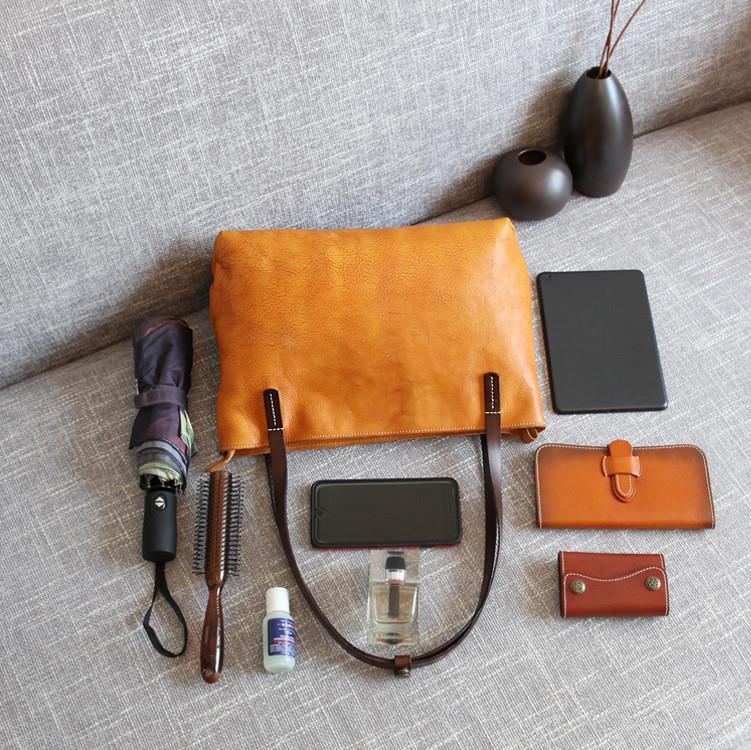 Large brown leather tote bag with dark handles on a sofa, surrounded by daily essentials like a wallet, tablet, phone, umbrella, hairbrush, perfume, and sanitizer.
