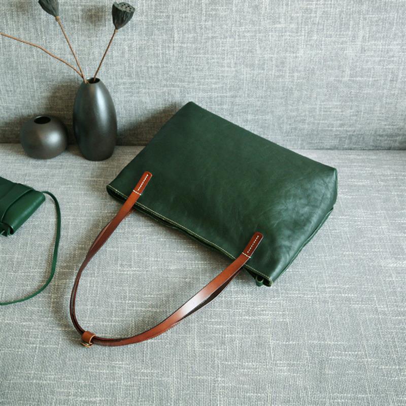 Large green leather tote bag with brown handles on grey sofa, minimalist vases nearby