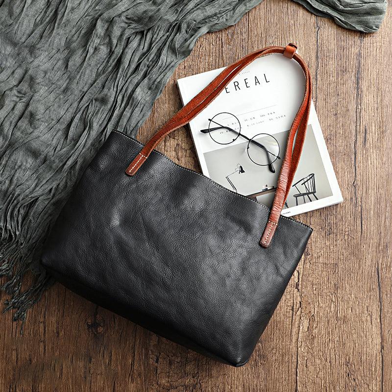 Black full grain leather tote bag with brown handles on wooden surface, stylish and spacious handbag for women