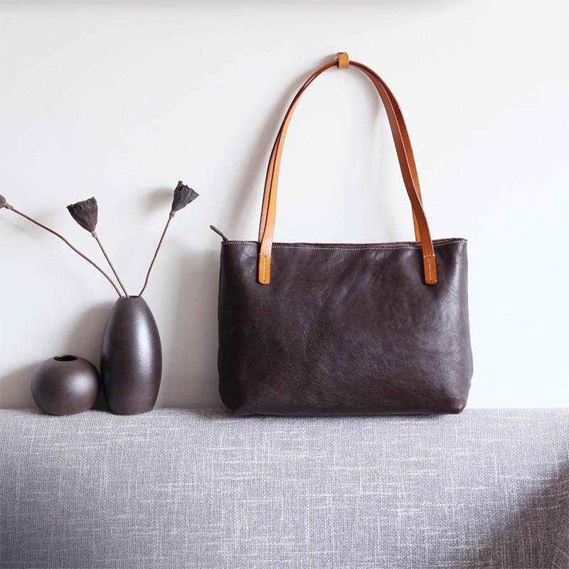 Black full grain leather tote bag with brown straps on a grey sofa, minimalist decor