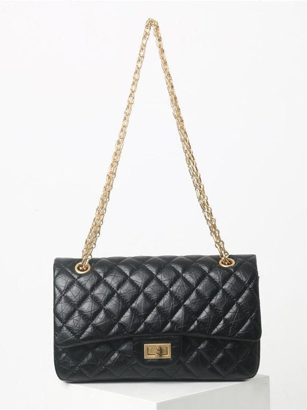 Woman in white shirt carrying black quilted leather shoulder bag with gold chain strap