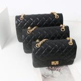 Woman in white shirt carrying black quilted leather shoulder bag with gold chain strap