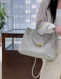 Woman holding a large grey woven leather handbag with gold clasp, modern indoor setting