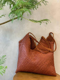 Brown woven leather hobo tote bag with braided handles on a wooden table, indoor setting