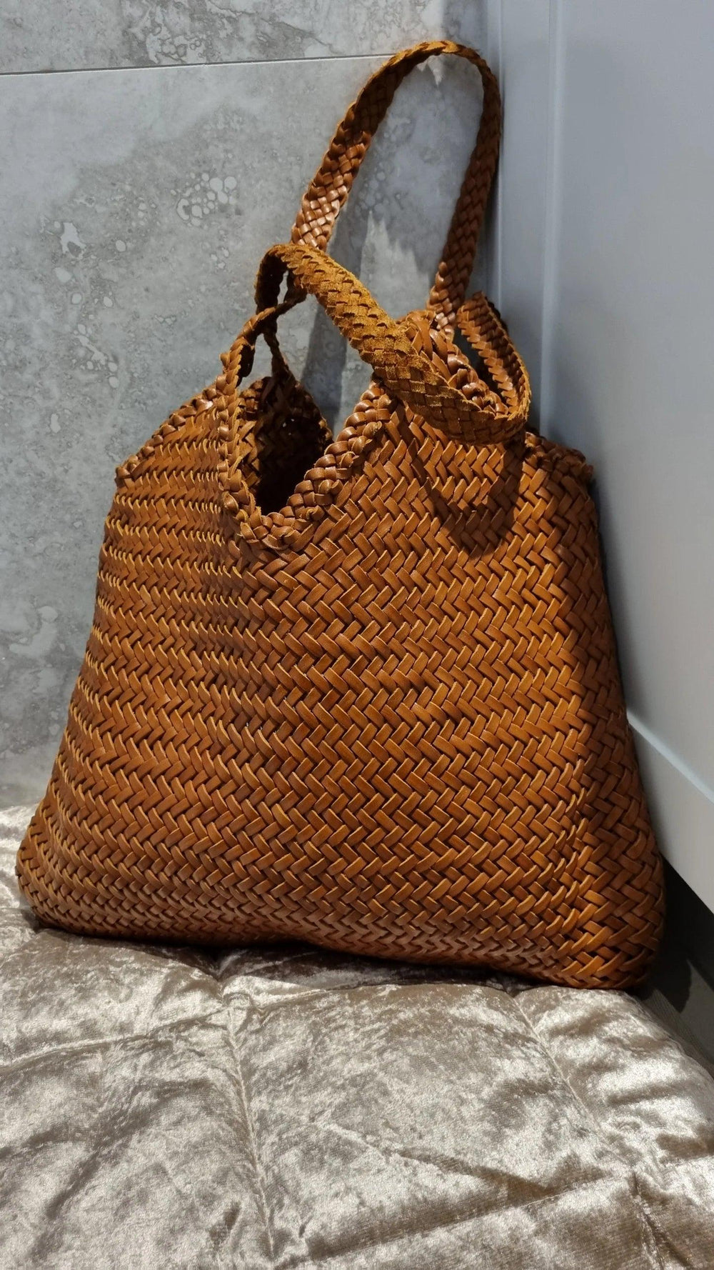 Brown woven leather tote bag with double handles on a grey textured surface