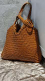 Brown woven leather tote bag with double handles on a grey textured surface