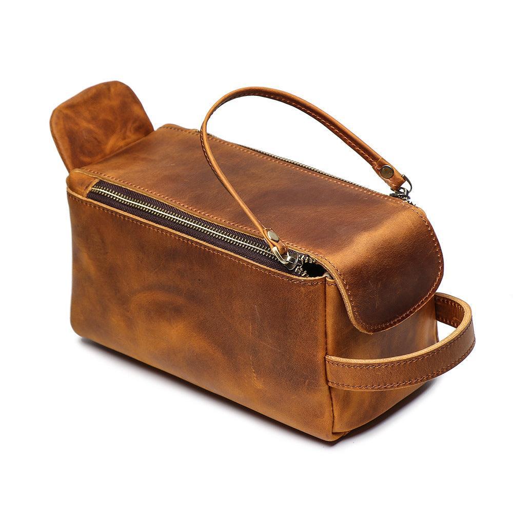 Brown genuine leather toiletry bag with zipper, side handle, and top strap on white background