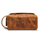 Brown genuine leather toiletry bag with gold-tone metal feet and side handle on white background