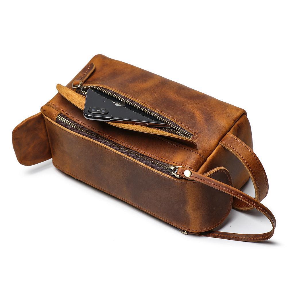 Brown genuine leather toiletry bag with dual zippers and a wrist strap on white background