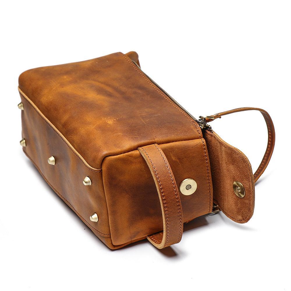 Brown genuine leather toiletry bag with zipper closure, metal studs, and wrist strap on white background