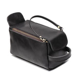 Black genuine leather toiletry bag with handle and gold zipper on white background