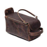 Brown genuine leather toiletry bag with zipper, handle, and flap closure on white background.