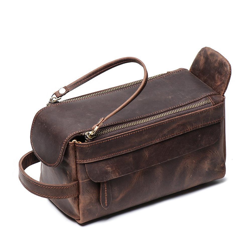 Brown genuine leather toiletry bag with top zipper, side handle, and front pocket on white background