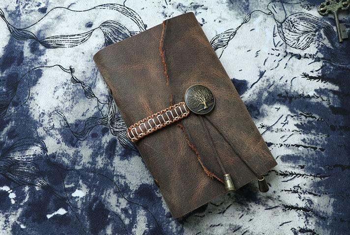 A6 vintage leather sketchbook diary with tree emblem and stitched wrap closure on fabric background