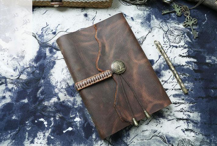 Vintage brown leather diary journal with tree emblem button and woven strap on artistic background