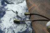 Close-up of vintage brown leather journal with wrap tie on patterned fabric background.