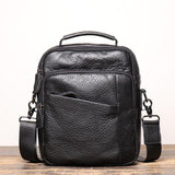 Men's black leather crossbody shoulder bag with handle and front pockets on wood surface
