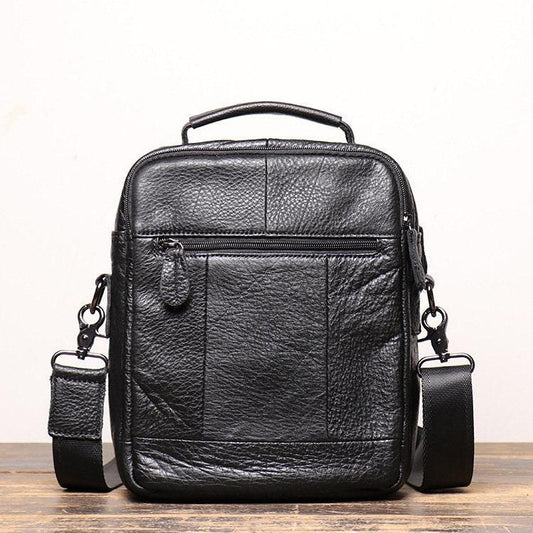 Black leather men's crossbody shoulder bag with front zipper pocket on wooden surface