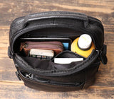 Open black leather men's crossbody shoulder bag with phone, wallet, drink, and book inside on wooden table