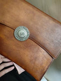 Handcrafted brown leather clutch bag with decorative metal clasp, held in hand