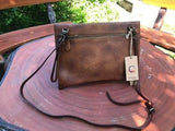 Handcrafted brown leather clutch bag with shoulder strap on a round wooden table outdoors