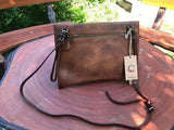 Handcrafted brown leather clutch bag with shoulder strap on a round wooden table outdoors