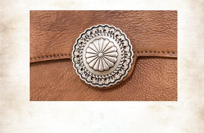 Close-up of brown handcrafted leather clutch with ornate silver button clasp