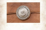 Close-up of brown handcrafted leather clutch with ornate silver button clasp