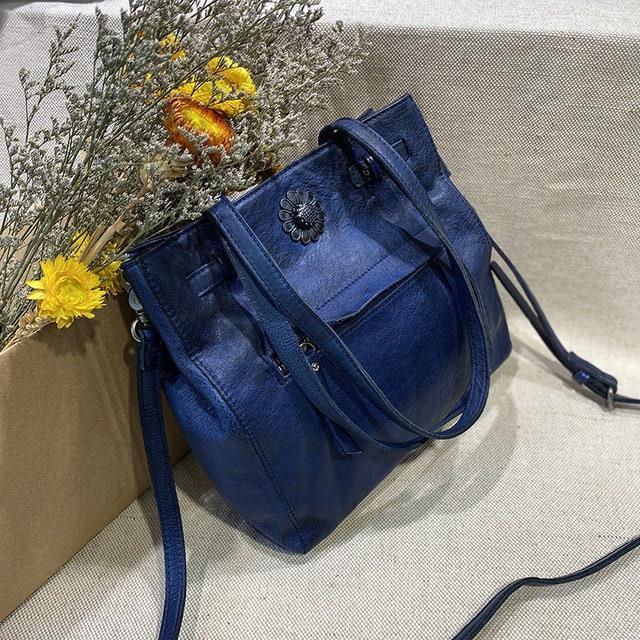 Blue leather shoulder bag with floral emblem, large tote style, styled with dried flowers