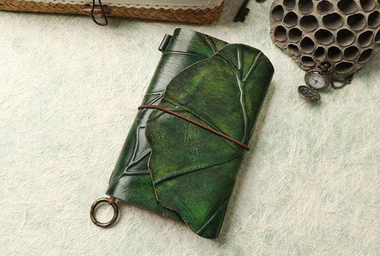 Handcrafted green leather journal with embossed leaf design and elastic closure on a textured background