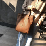Woman carrying a large brown full-grain leather tote bag with double handles