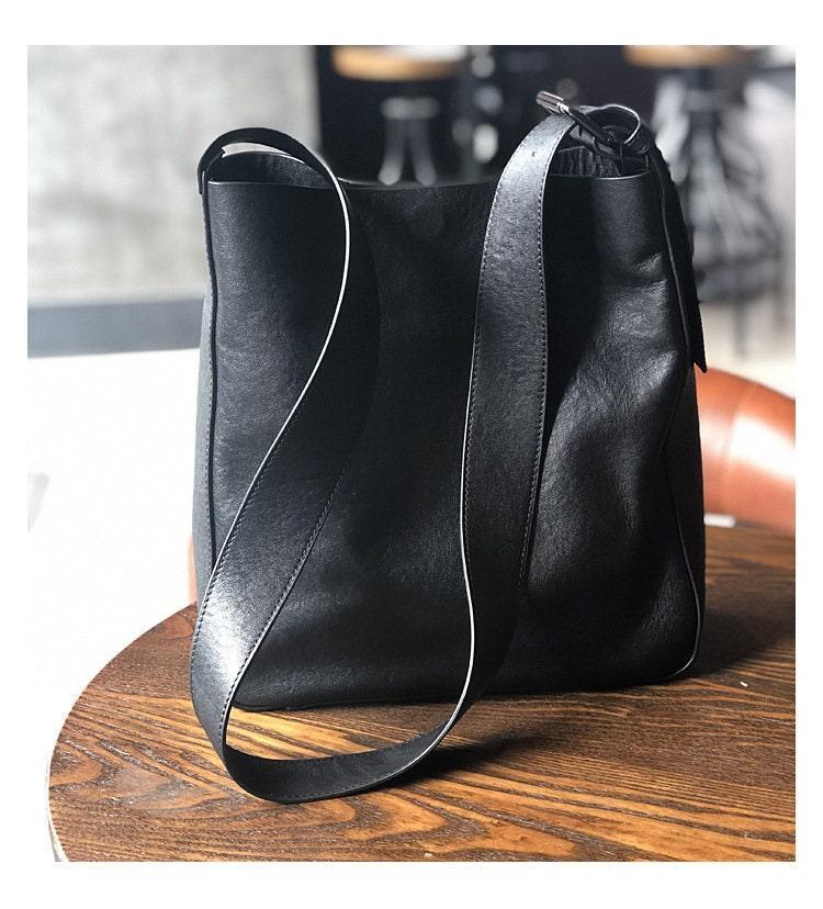Black full grain leather shoulder bag with wide strap on wooden table