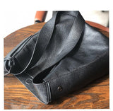 Black full grain leather shoulder bag with wide strap on wooden table