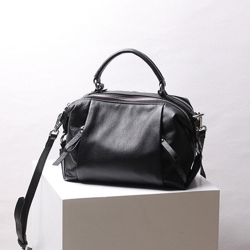 Black genuine leather handbag with top handle and shoulder strap on white display block